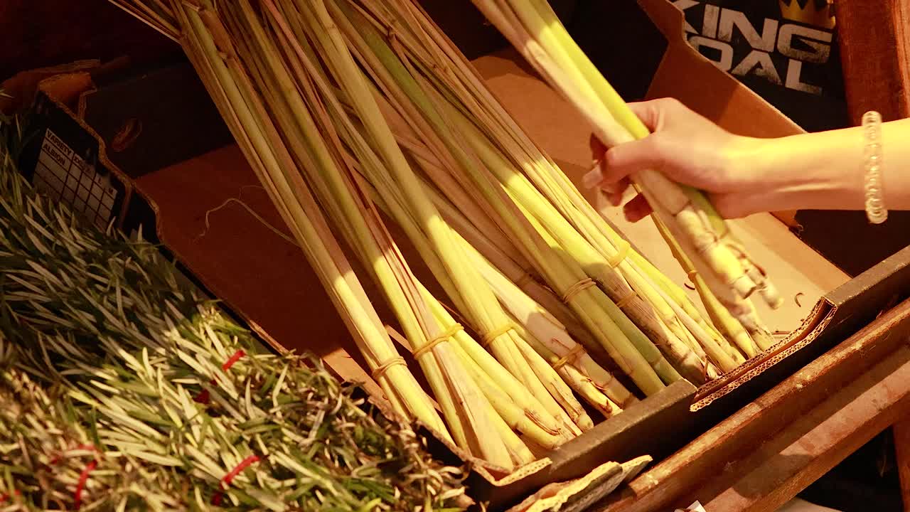 A hand examines and selects lemongrass stalks in a warmly lit supermarket setting