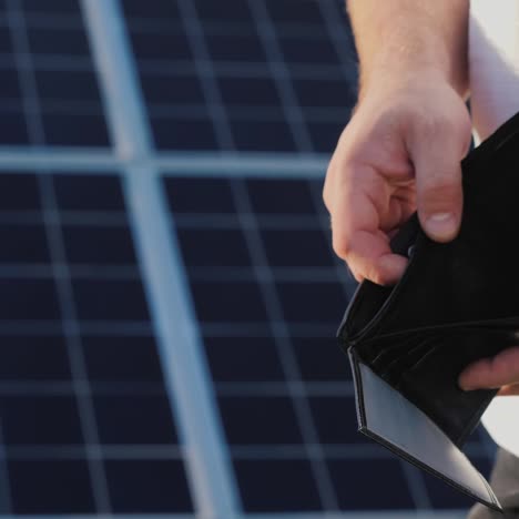 a man holds an empty purse against the background of solar panels