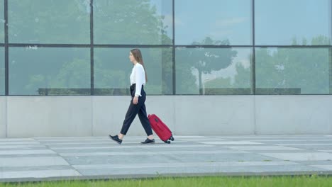 Corporate-woman-walks-with-red-trolley-in-front-of-office-building