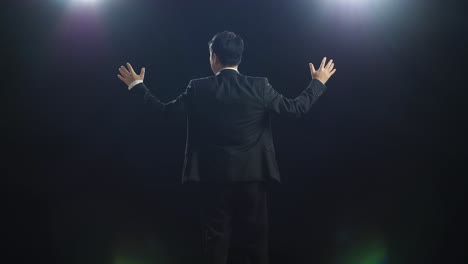 back view of asian speaker man in business suit spreading out his arms in the black screen studio