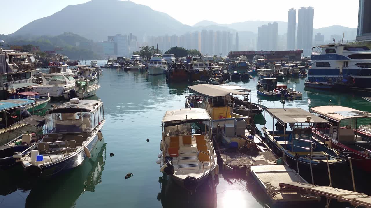 vista frontal de varios barcos mantenidos en el puerto en el refugio de tifones con colina y edificios en el fondo en lei yu mun, hong kong