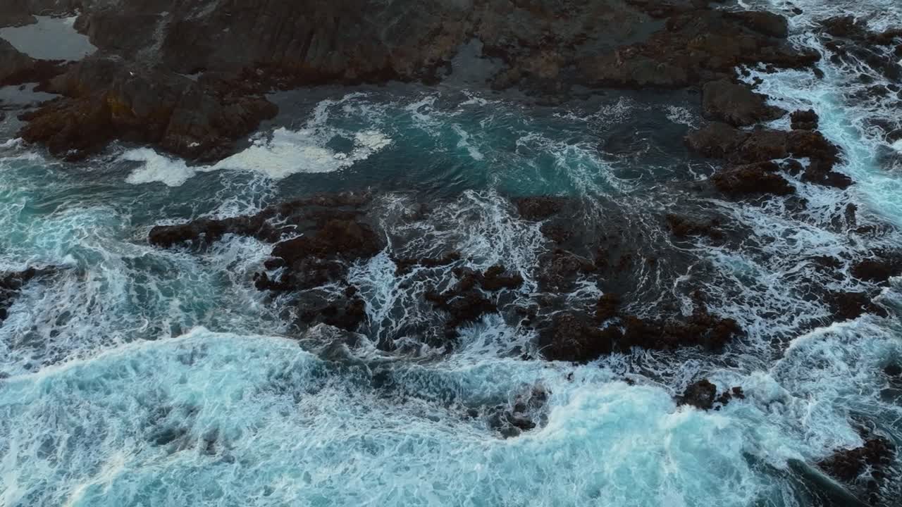 Vista aerea dall'alto di onde che si infrangono su un letto di rocce creando pozze di marea