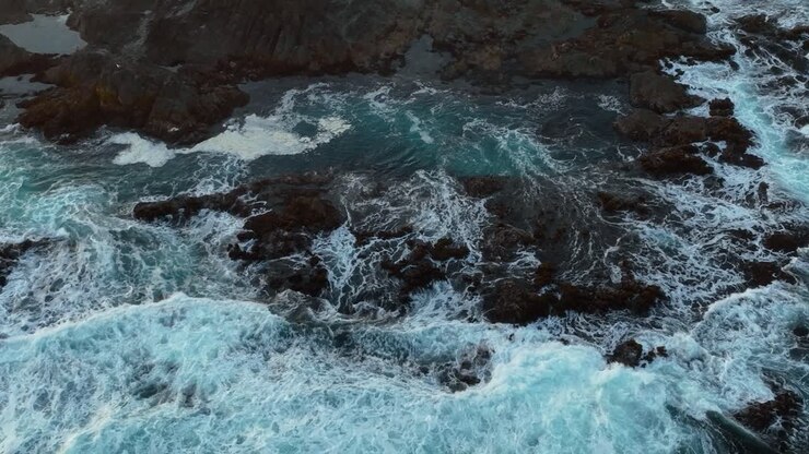 Vista aerea dall'alto di onde che si infrangono su un letto di rocce creando pozze di marea