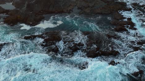 top down aerial view of waves crashing into a bed of rocks creating tide pools