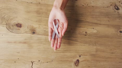 Video-of-hands-of-caucasian-woman-holding-white-ribbon-on-wooden-background