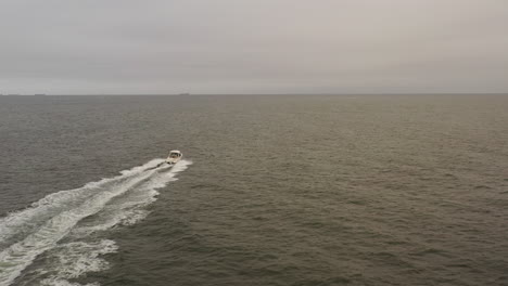 an aerial view of a small, white fishing boat speeding in the deep atlantic ocean out by long island, ny