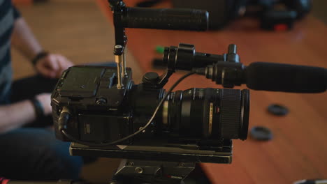 close-up of camera tripod quick release plate on wooden table. two lens caps placed nearby. background includes couch and soft indoor lighting creating a relaxed environment