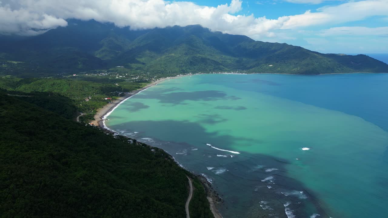 A slow forward aerial shot of the sea in Dingalan, Aurora, gliding above turquoise and deep blue waters with waves rolling toward the rugged coastline framed by lush green hills