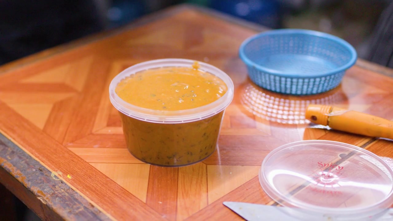 Close-up shot of a chef pouring steaming orange curry into a takeaway container outdoors.