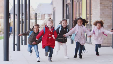 happy young school kids wearing coats and bags running in a walkway outside their school building