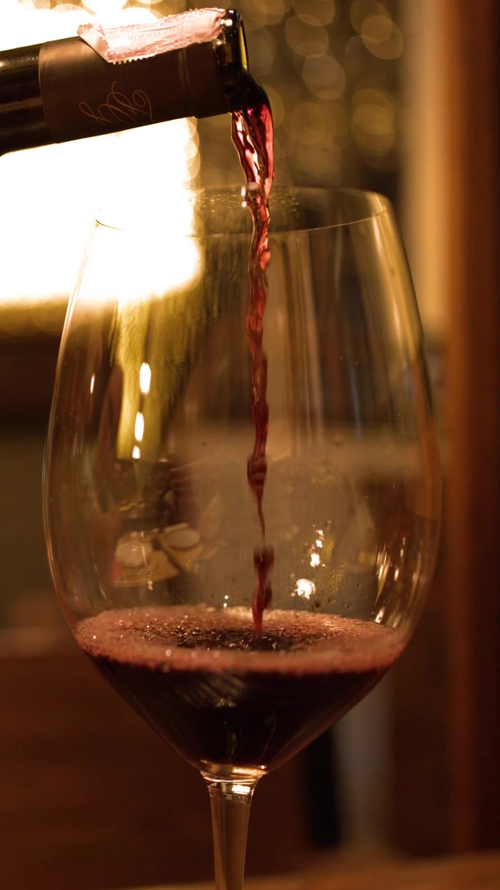 Un sumiller sirve vino tinto en una copa de cristal con un cálido fondo bokeh