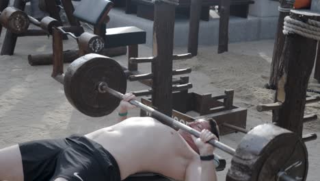 Young caucasian muscular man lifting weights in an outdoor gym on the beach in Thailand.