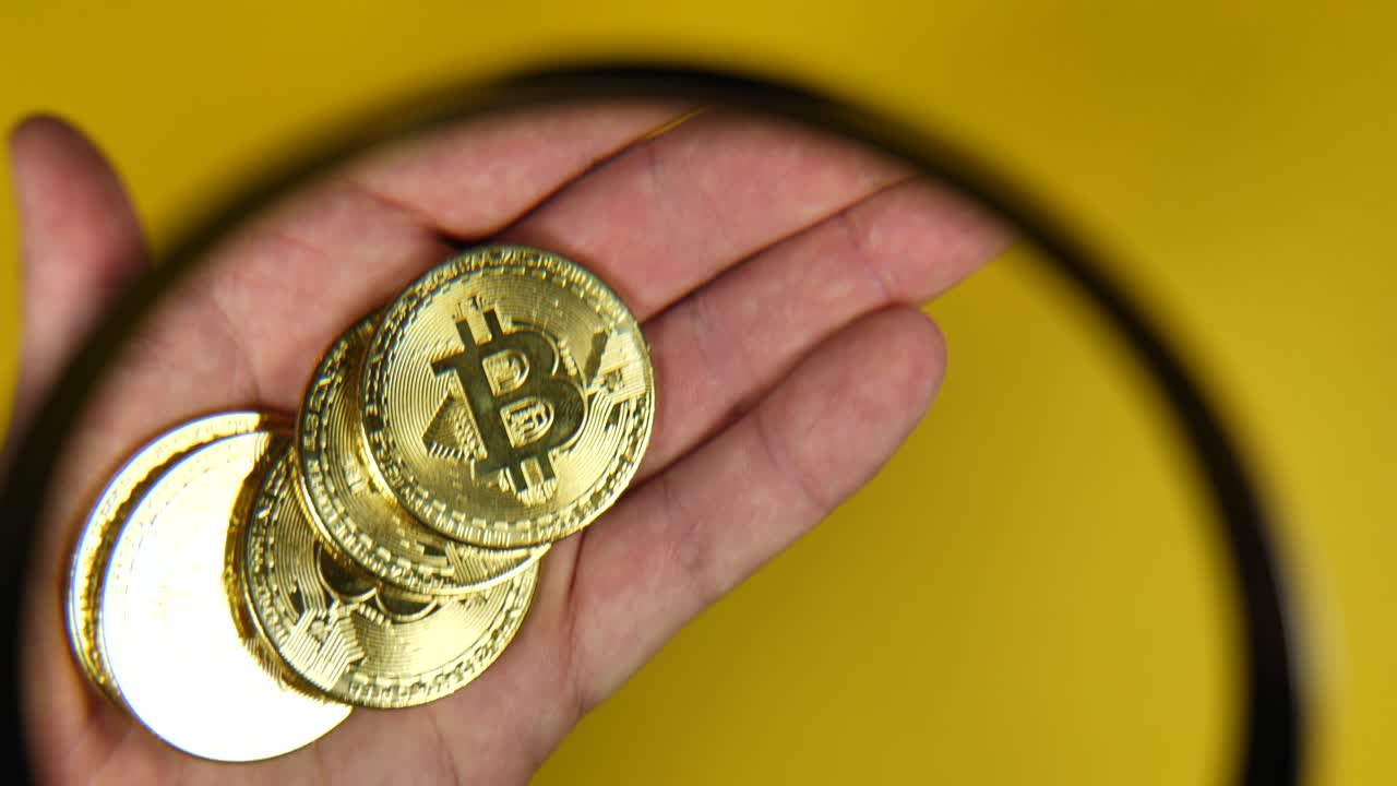 cerca de una persona mirando a través de una lupa de mano con bitcoins dorados, inversión