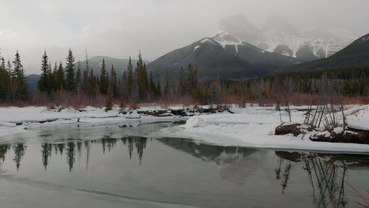 mañana nebulosa en canmore, alberta, canadá con las icónicas montañas tres hermanas envueltas en nieve, mientras que un tranquilo estanque adorna el primer plano, ofreciendo un vistazo a la belleza etérea de la naturaleza