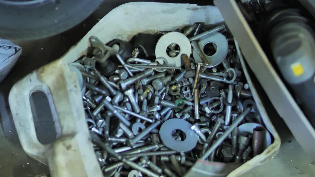 Close up of dirty reused jug filled with bolts and metal parts on cement floor
