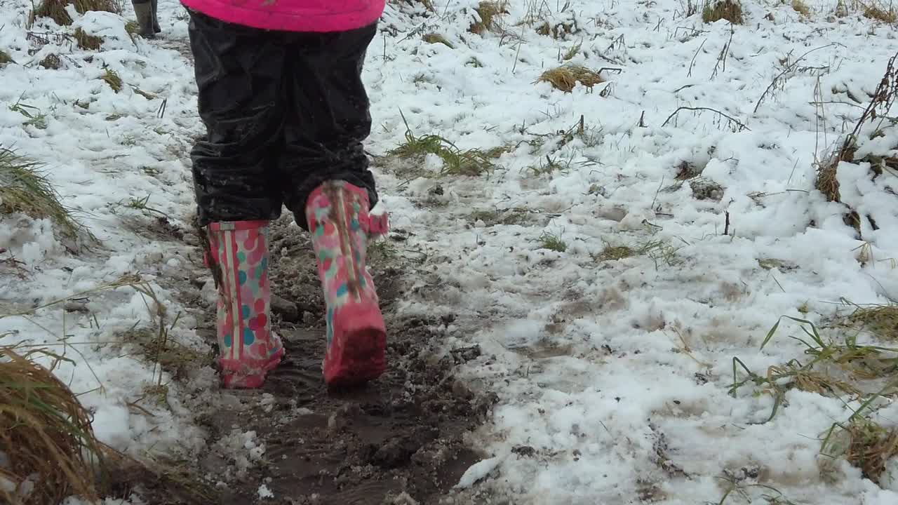 Niño caminando en cámara lenta con botas de agua en un campo nevado