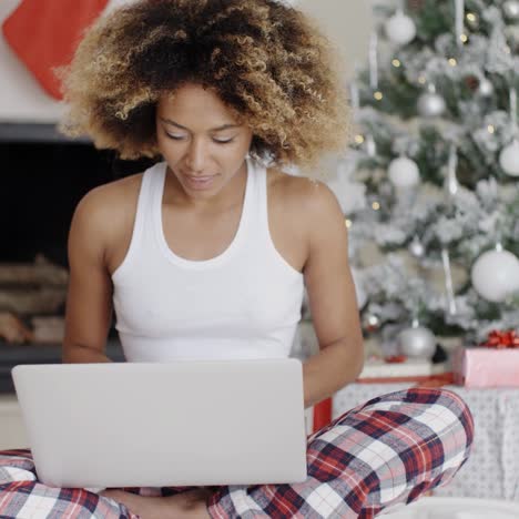 mujer usando una computadora portátil frente al árbol de navidad