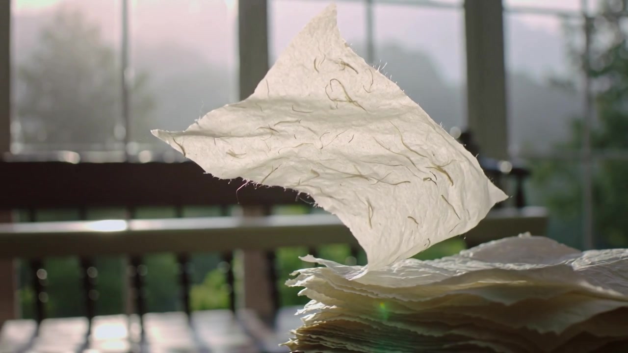 Lifting sheer paper sheet by breeze from stack on table at sunlit porch, gliding, revealing fibers