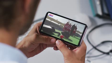 compuesto de un médico masculino viendo un partido de hockey en un teléfono inteligente