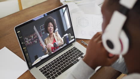 african american businessman sitting at desk using laptop having video call with female colleague
