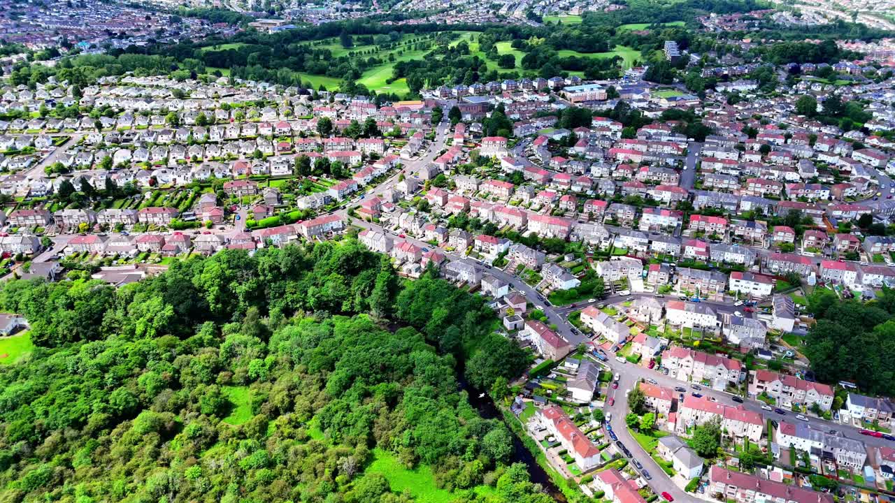Aerial view of typical UK suburban housing estate beside green woodland and parkland. Modern residential neighborhood blending with surrounding nature landscape