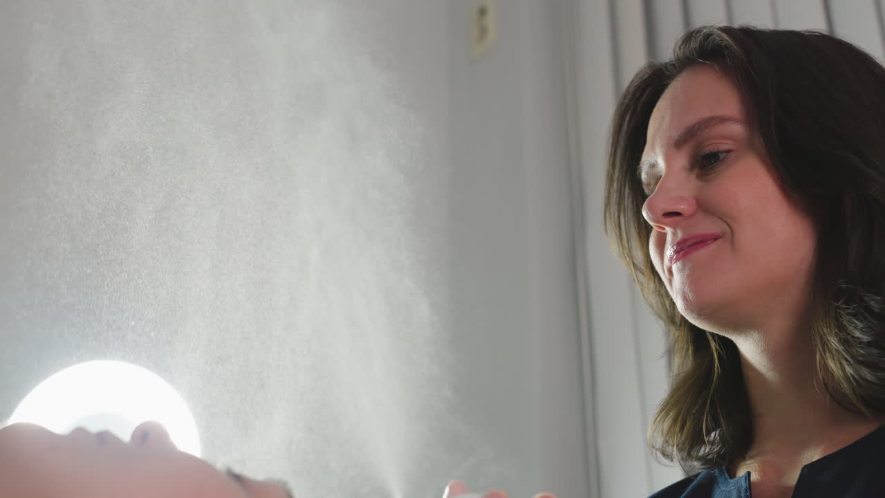 Skin care specialist spraying fine hydrating mist onto face of female client under bright spa light for refreshing boost and soothing relaxation during rejuvenating facial treatment session