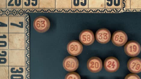 cinematográfico primer plano giratorio suave zoom hacia fuera disparado desde arriba de un bingo barriles de madera en un círculo, figuras de madera, viejos números de fondo, juego de mesa vintage, iluminación profesional, cámara lenta 4k