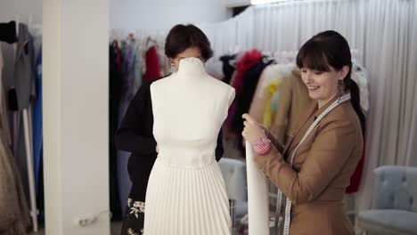 two professional tailors, designers working with new model tailoring dress on mannequin in studio, atelier. fixing sleeves, cheerfully smiling. fashion and tailoring concept