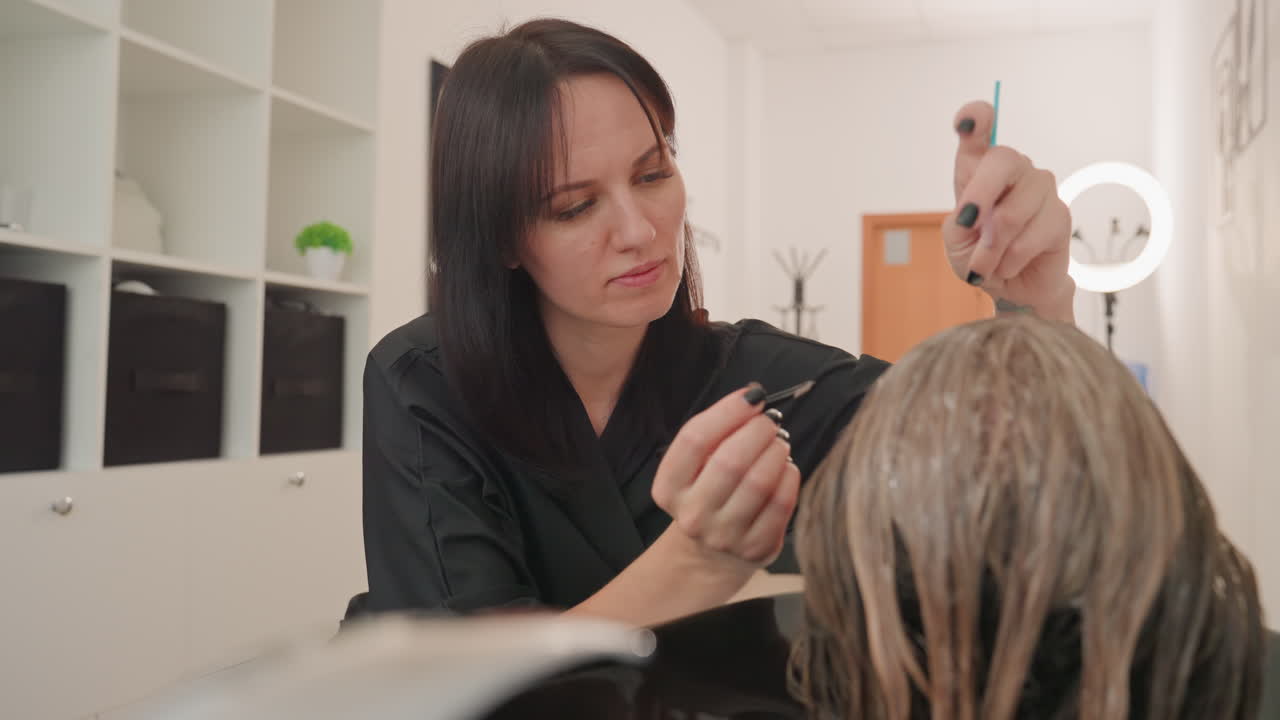 Peluquero examinando el pelo mojado en el lavabo, comprobando suavemente la saturación del producto y separándolo por secciones para el tratamiento; interior de un salón íntimo con espejo, armarios, iluminación cálida y herramientas profesionales a la vista.