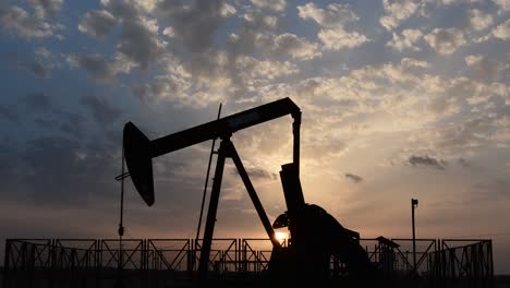 Silhouette-of-crude-oil-pump-standing-still-in-the-oilfield-at-cloudy-sunset