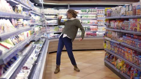 Full-length-footage-of-young-woman-dancing-through-grocery-store-aisles.-Excited-woman-having-fun,-dancing-supermarket.-Slow-motion