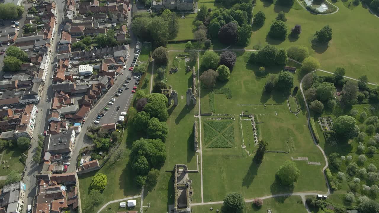 Aerial view of the Glastonbury Abbey ruins an 8th century monastery and gardens. Drone moving forwards over the ruins in direction to the town and with some buildings on the left side. 4K, 60fps.