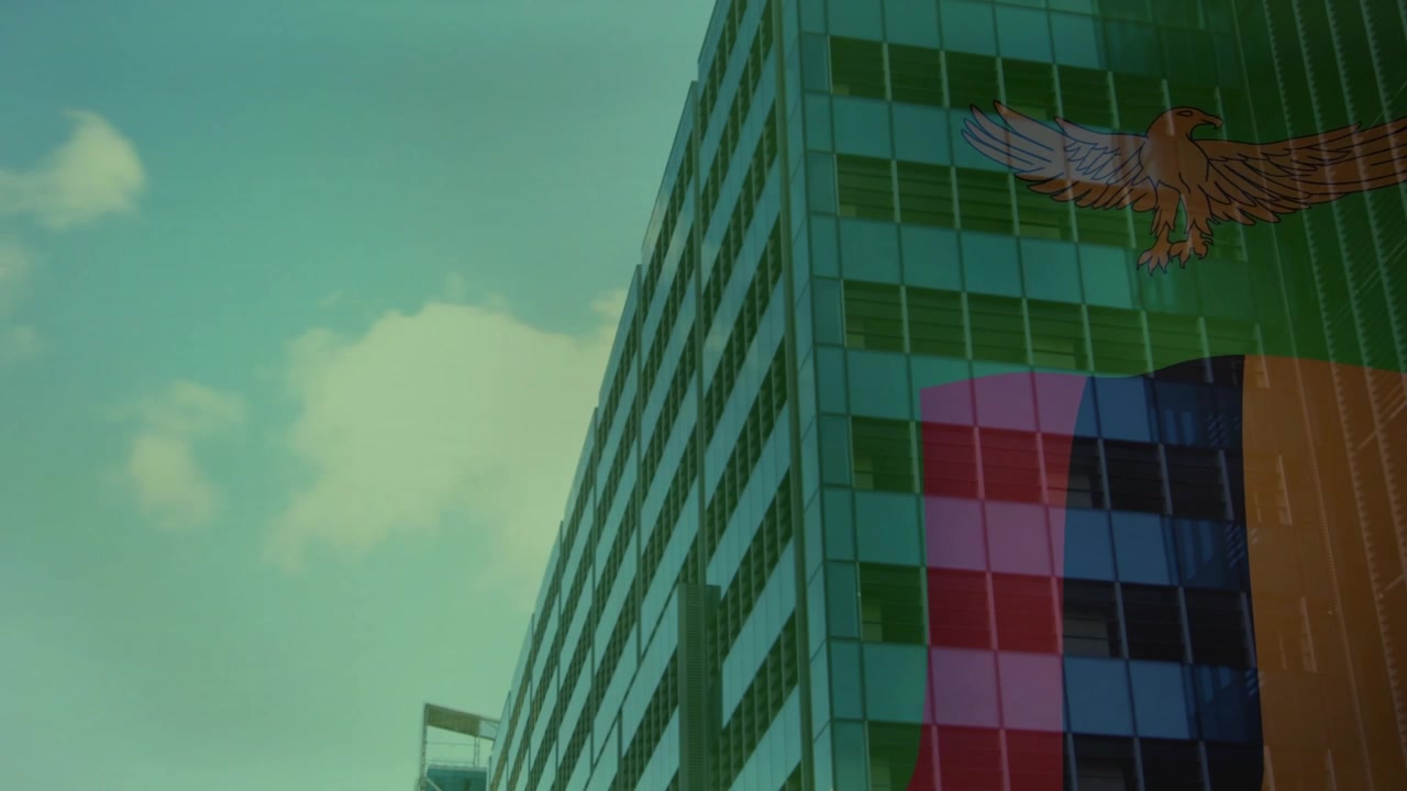 Cámara paneando hacia arriba a la derecha, mostrando la fachada del edificio, bloques de color y un emblema de águila, con una nube a la deriva.