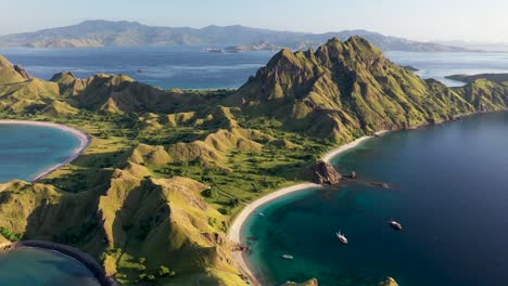 Panorama-De-La-Isla-De-Padar-Indonesia-Con-Botes-Turísticos-Debajo-Y-Komodo-En-El-Fondo,-Tiro-Aéreo-A-La-Derecha