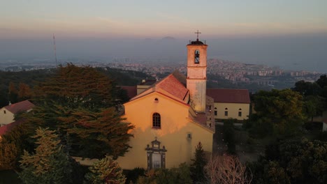 drone zooming out from church nestled in lush sardinian forest, revealing breathtaking sunset over tranquil landscape and highlights the serene surroundings