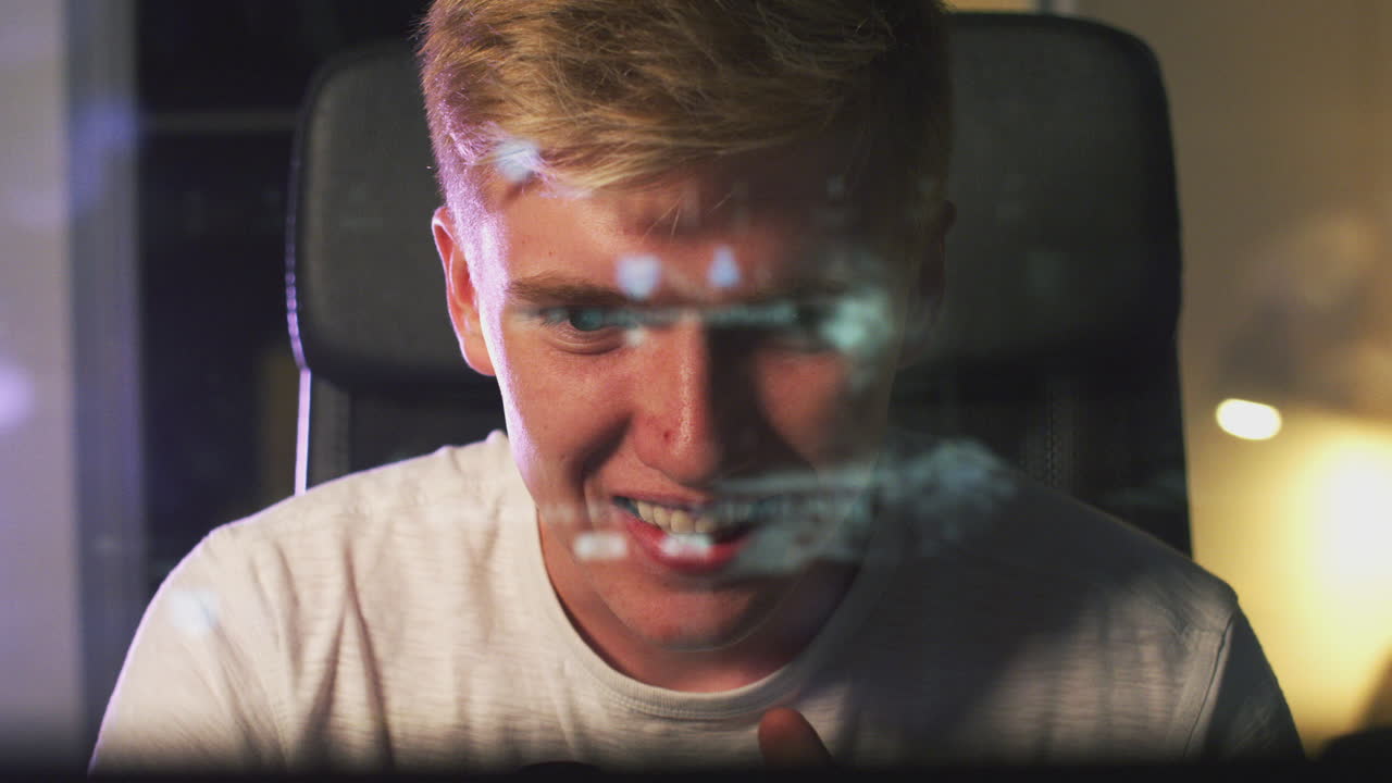 мальчик-подросток играет дома с экраном компьютера, отраженным в его лице.