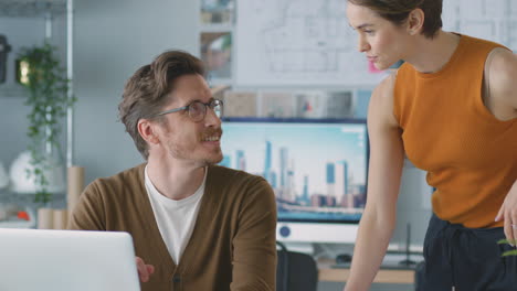 Male-And-Female-Architects-In-Office-Working-At-Desk-On-Laptop-And-Looking-At-Plans