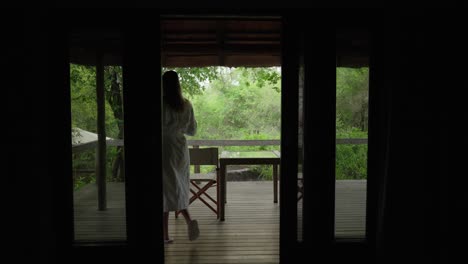 a woman walking outside onto the deck of a safari lodge with a cup of coffee