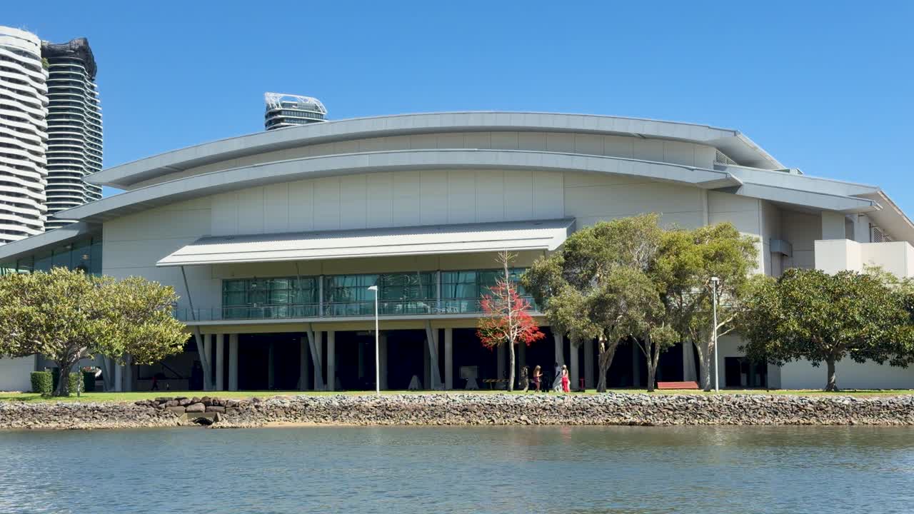Wide shot of modern convention center by river, static camera, bright daylight, urban background