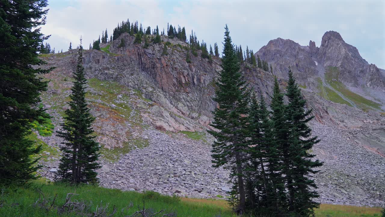 Capitol Peak wilderness camping campsite Mt Daly sunset dusk Colorado summer Aspen Snowmass last light Rocky Mountains Elk Range trailhead hiking high elevation clouds trees above treeline pan left