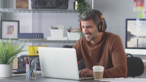 businessman in office listening to music on wireless earphones  whilst working on laptop