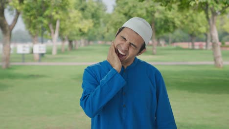 sick muslim man suffering from tooth pain in park