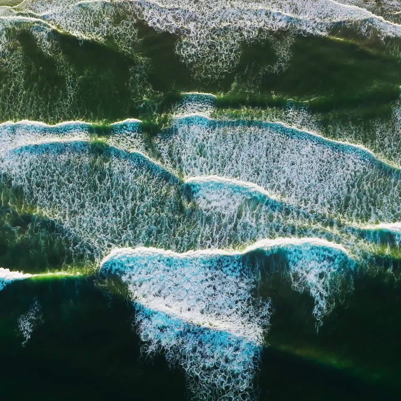 Amazing beautiful waves moving the sandy beach of Morro Bay, California, USA. White foamy tide slowly moving to the shore. Bird's eye view