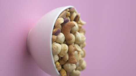 nueces mezcladas en un cuenco blanco sobre un fondo rosa