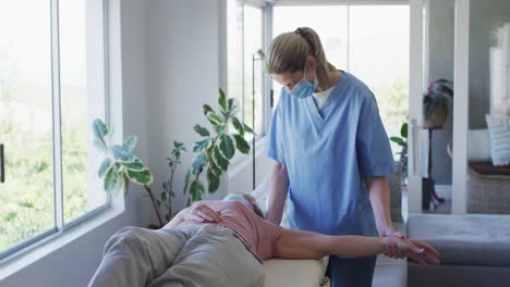 Female-health-worker-stretching-arm-of-senior-woman-at-home