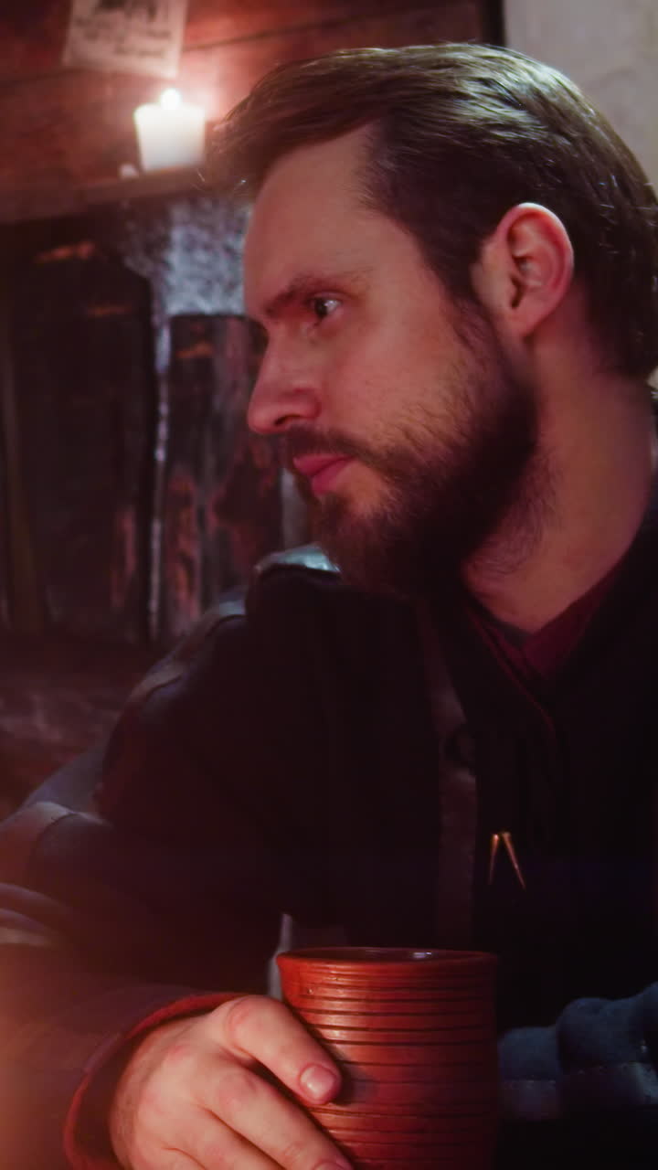 Man punches table with fist near friend in medieval tavern. Angry guy complains on life and drinks alcohol with fellow in old inn. Emotional guest rests in bar