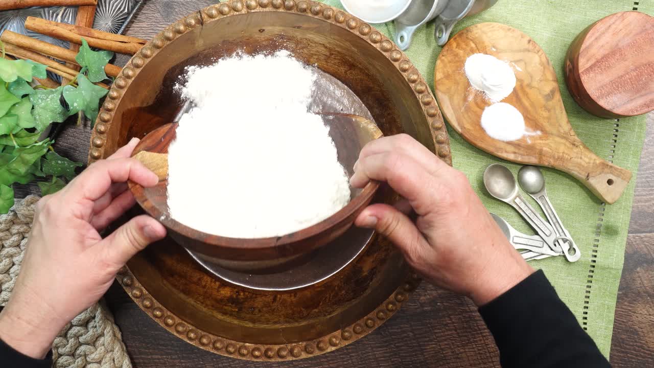 Baking a carrot cake loaf with cream cheese icing and topped with roasted salted pecans. Making a Autumn dessert with carrots, flour, sugar, nuts and frosting. Adding flour to the carrot cake batter.