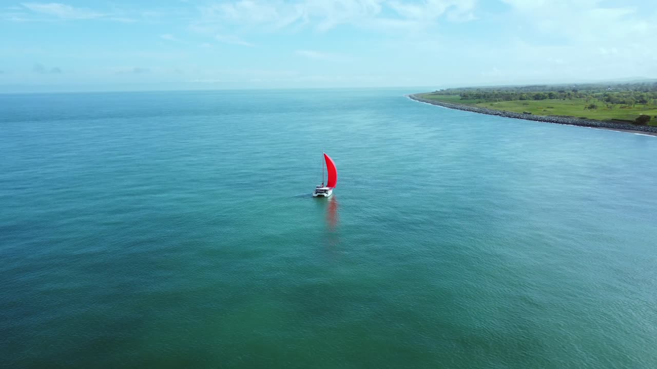 antena dando vueltas alrededor de un velero de vela roja con vistas a la costa