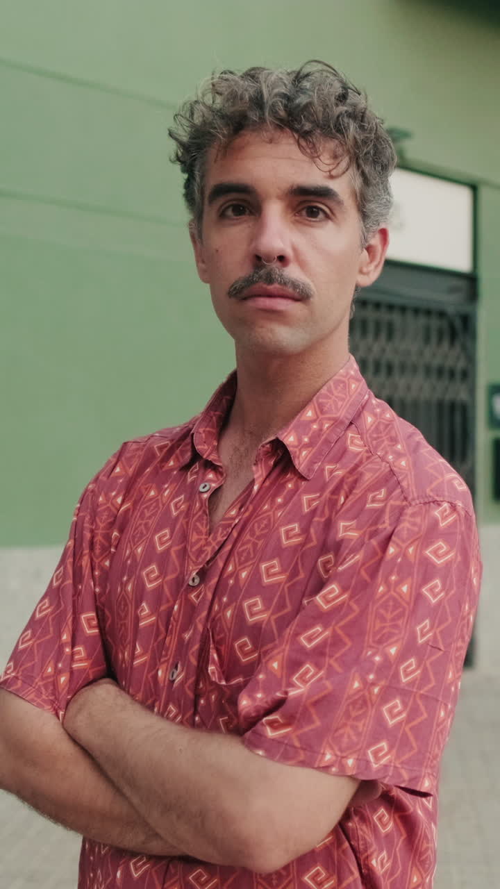 Homem confiante com bigode e cabelo encaracolado em pé com os braços cruzados