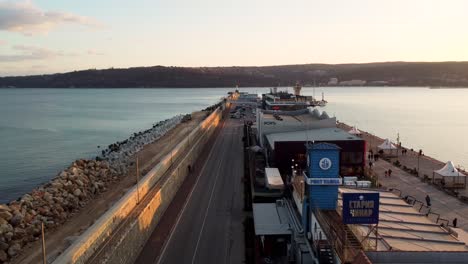 Drones-Volando-Sobre-El-Puerto-De-Varna-Durante-La-Puesta-De-Sol-Con-Autos-Pasando